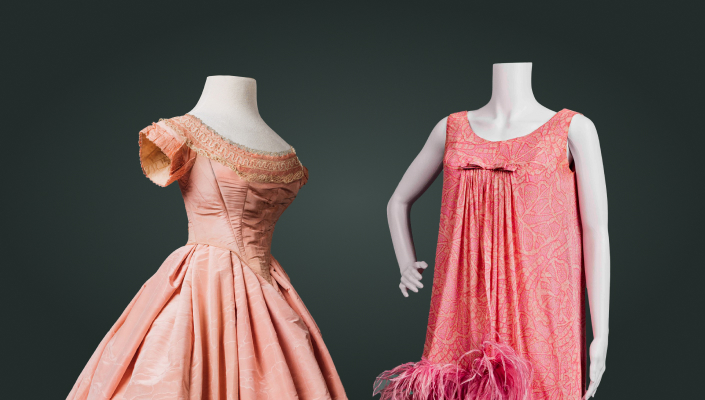 Two pink dresses are shown. One, a formal ball gown with short sleeves from the 1860s, the other a short, sleeveless cocktail dress with ostrich feather trim, from the 1960s.