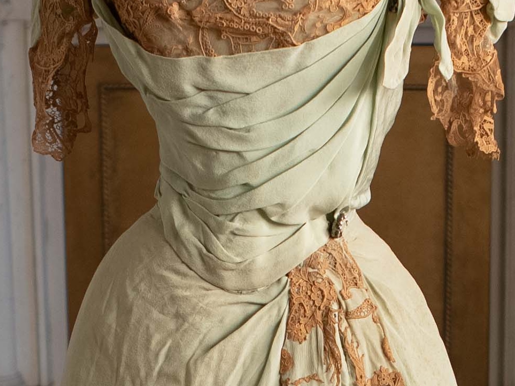 At the mid-section of an ornate gown, a small rhinestone brooch adorns the folded pale green silk.