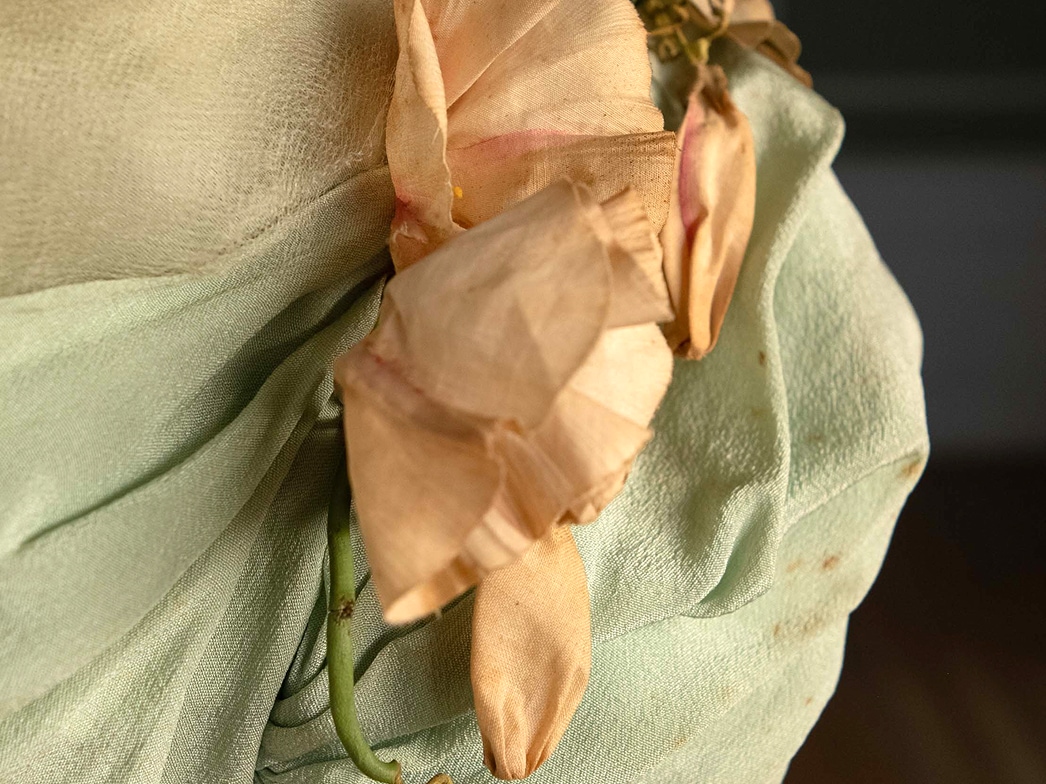 Pale cream and pink silk flowers adorn the shoulder of a sleeve.