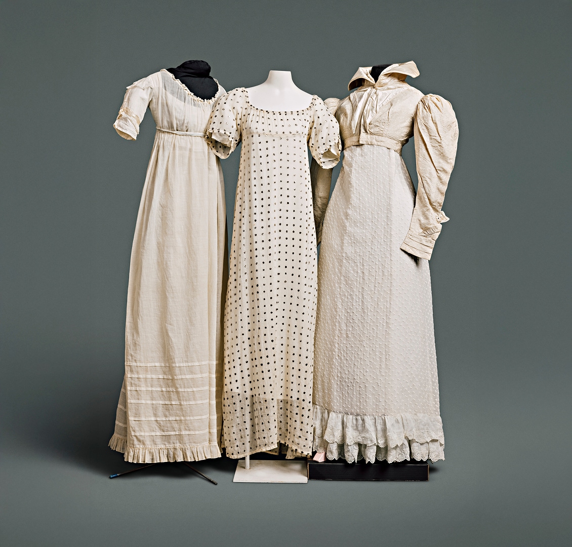 Three cotton dresses with simple patterns and sleeves extending to just above the elbow. One of the dresses is accompanied by a cotton Spencer jacket with high collar covering the neckline.