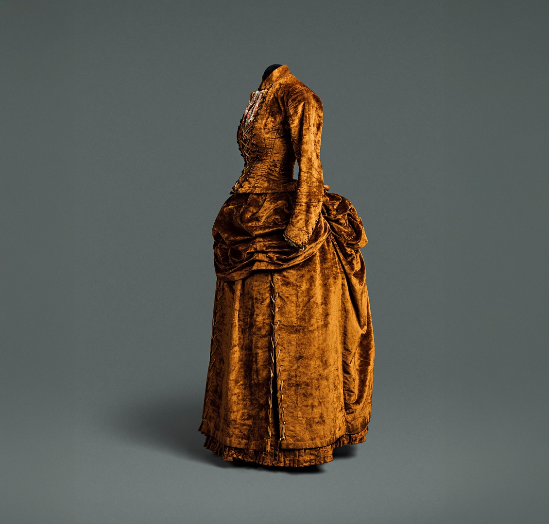 A dark ochre dress consisting of a separate bodice and skirt. The dress is accented with decorative brown buttons extending down the front of the bodice which is laced together with a gold cord.