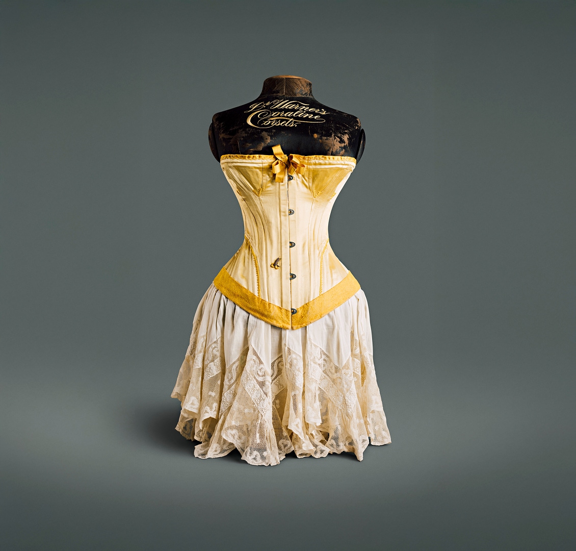 A canary yellow silk corset with bow at the bosom, plush hemline, and metal fastening hooks.
