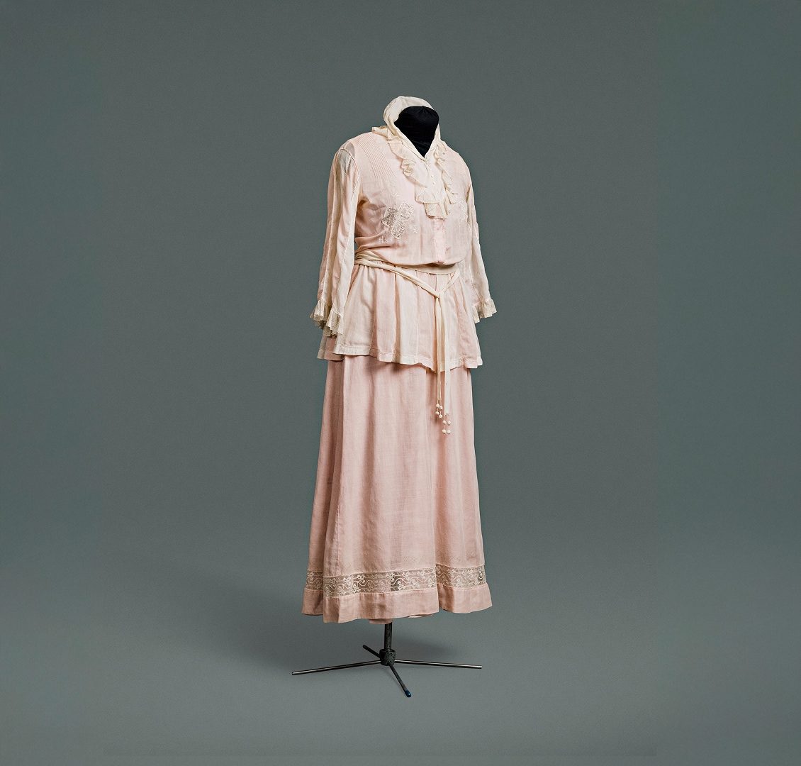 A simple pink cotton one-piece dress designed to appear to be a suit composed of a jacket over a blouse, worn with a matching skirt.