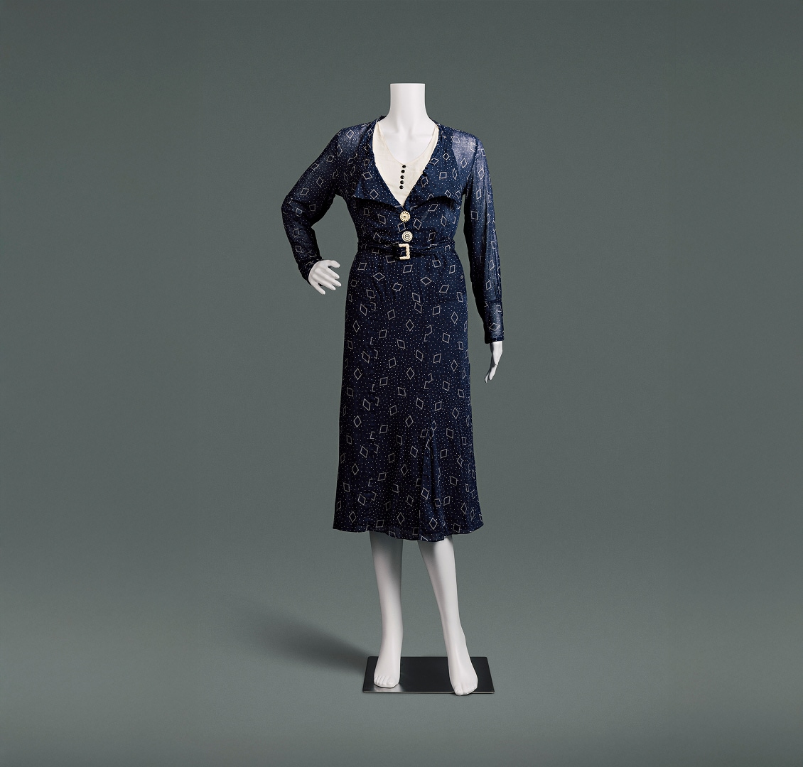 A slim fitting, midnight blue cotton dress with a high waist, and a skirt that comes down just below the knees. The material is covered with small polka dots and a diamond shaped pattern.