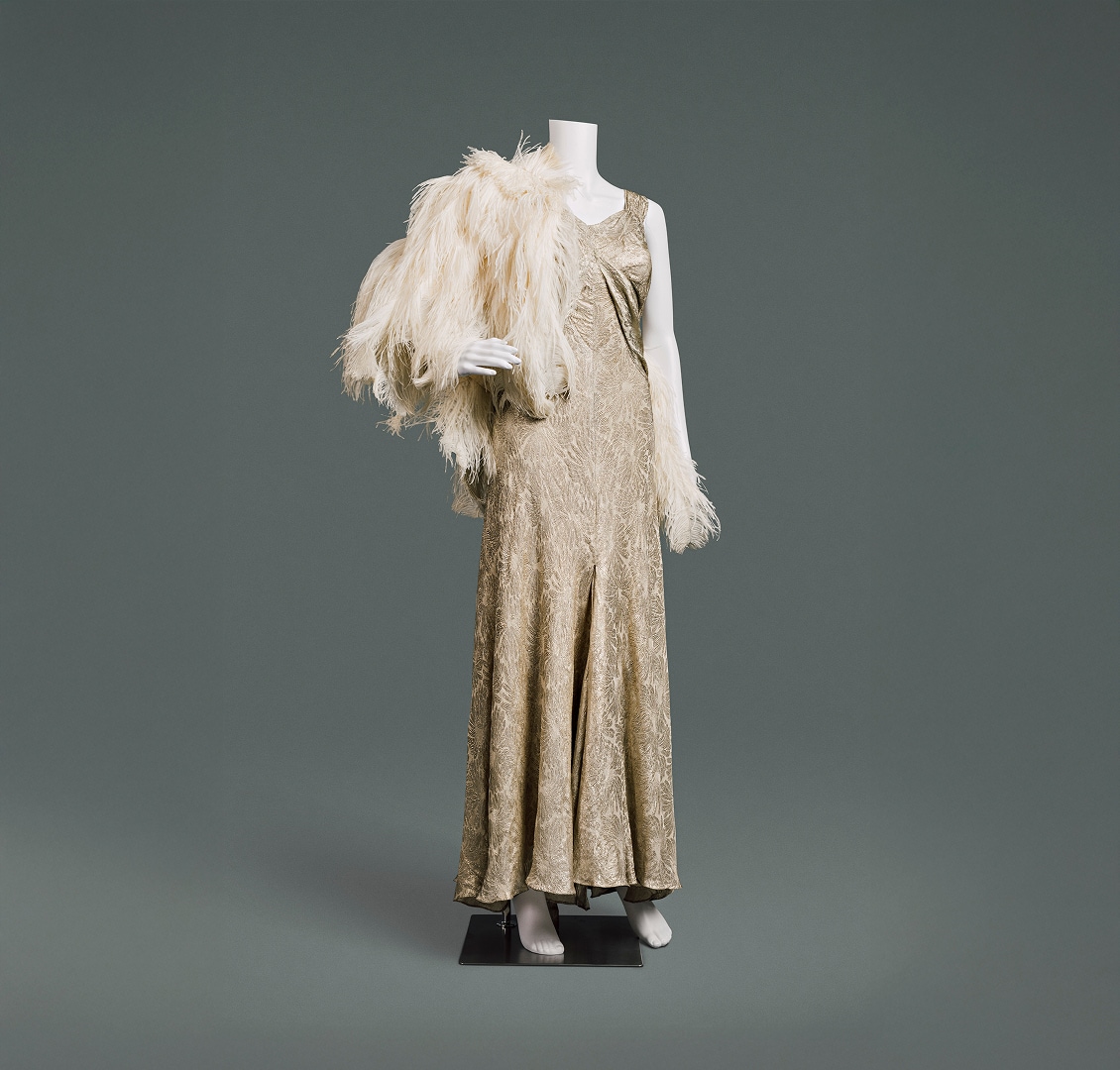 A glamorous gold-patterned silk lamé sleeveless evening gown with feather cape.