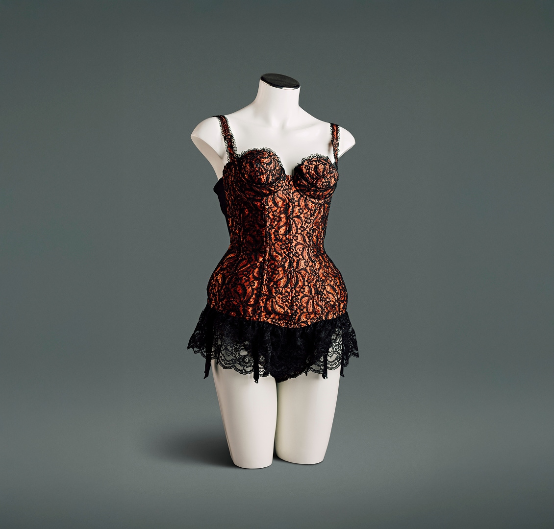 A nylon satin bustier with black lace overlay features a circle-stitched bullet bra with sling under-cups, power mesh elastic panels at both sides and the back, a deep lace flounce, and attached stocking suspenders.
