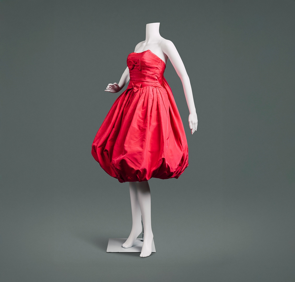 A cherry-red sleeveless silk cocktail dress with balloon skirt, sacque-back style, and red bows at the bosom and waist.
