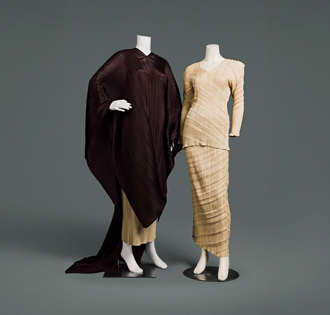 Two contemporary ensembles made of polyester. The first consists of a form-fitting, tan-coloured blouse and full length skirt, whose material is crinkled vertically and striped with horizontal diagonal shades. The second consists of a similar skirt mostly covered by a rich brown tunic blanketing the arms and body, extending below the knees in the front and trailing onto the floor like a long cape at the back.
