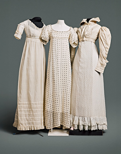 Three cotton dresses with simple patterns and sleeves extending to just above the elbow. One of the dresses is accompanied by a cotton Spencer jacket with high collar covering the neckline.