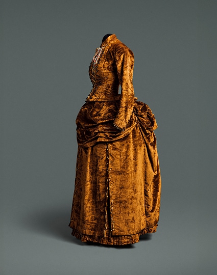 A dark ochre dress consisting of a separate bodice and skirt. The dress is accented with decorative brown buttons extending down the front of the bodice which is laced together with a gold cord.