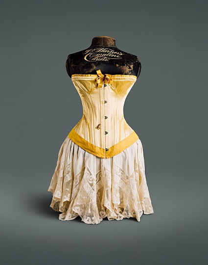 A canary yellow silk corset with bow at the bosom, plush hemline, and metal fastening hooks.