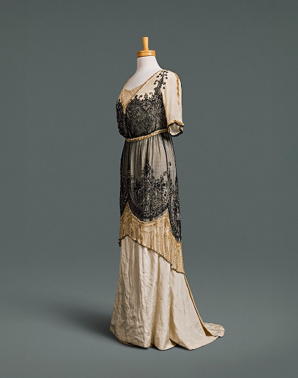 A long, narrow cream-coloured silk dress with low neckline and high waistline, overlayed with black and gold beaded tunic overskirt.