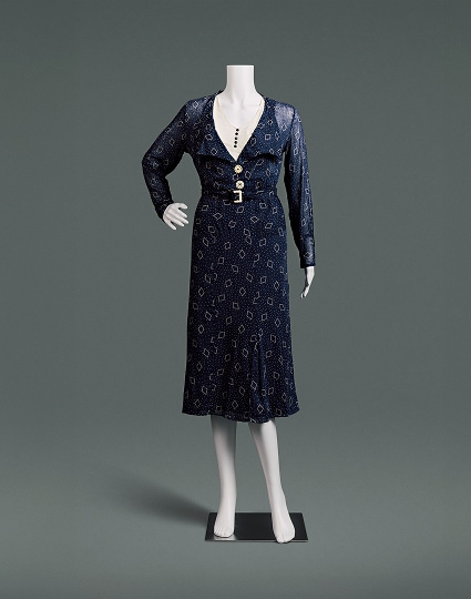 A slim fitting, midnight blue cotton dress with a high waist, and a skirt that comes down just below the knees. The material is covered with small polka dots and a diamond shaped pattern.