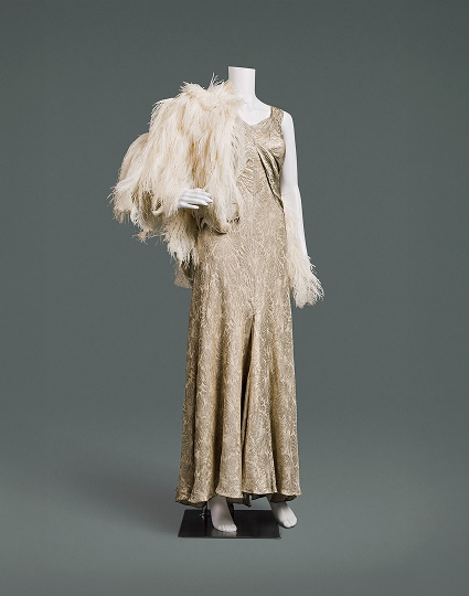 A glamorous gold-patterned silk lamé sleeveless evening gown with feather cape.