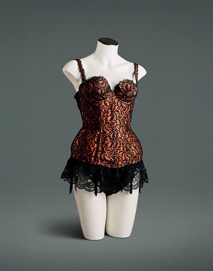 A nylon satin bustier with black lace overlay features a circle-stitched bullet bra with sling under-cups, power mesh elastic panels at both sides and the back, a deep lace flounce, and attached stocking suspenders.