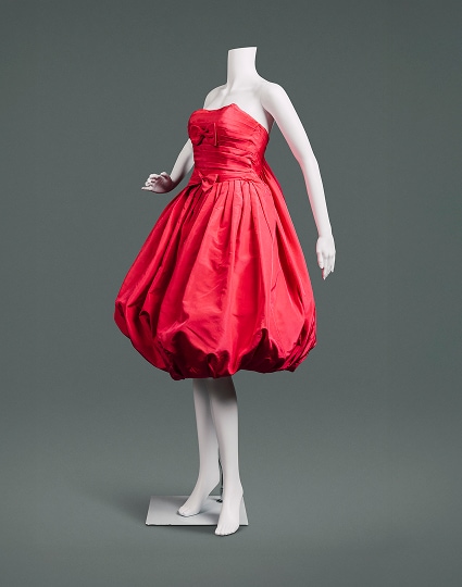 A cherry-red sleeveless silk cocktail dress with balloon skirt, sacque-back style, and red bows at the bosom and waist.