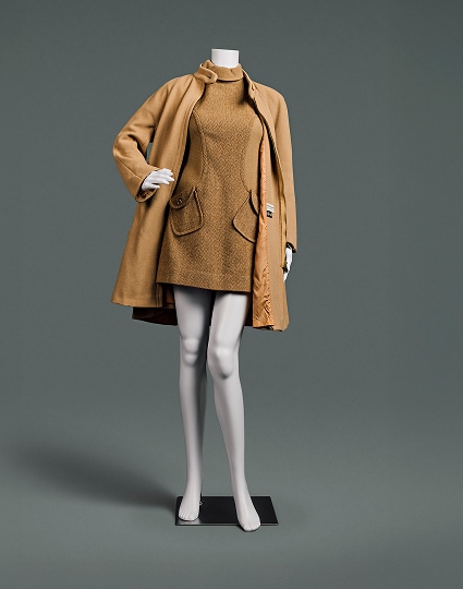 A very short camel-coloured, turtleneck wool dress with herringbone pattern and angled pockets accompanied by heavy camel coat that comes down to just above knee.