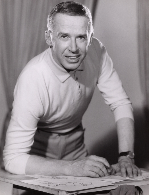 German fashion designer, Heinz Oestergaard, leans on his elbow, pen in hand, over a sketch book.