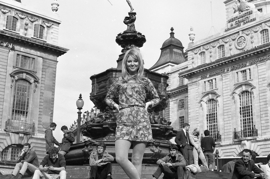 A model poses in a mini dress outdoors in London’s Piccadilly near the statue of Eros wearing a mini dress.