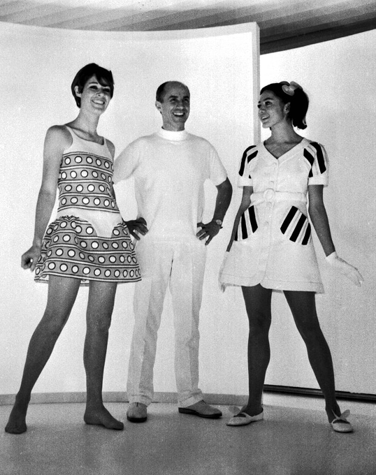 Fashion designer André Courrèges is flanked by two models wearing mini length dresses.