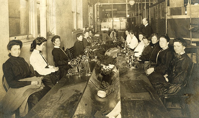 A long table with seamstresses working on both sides.