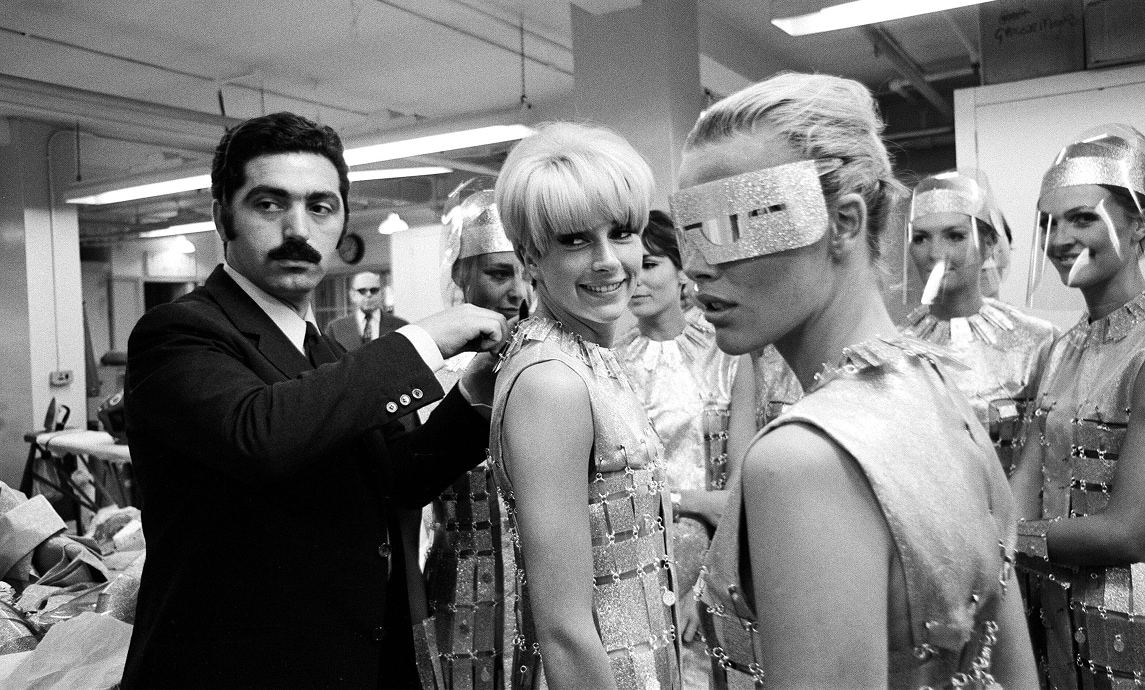 Paco Rabanne surrounded by actresses wearing his futuristic fashions, adjusts the neckline of one of the outfits.