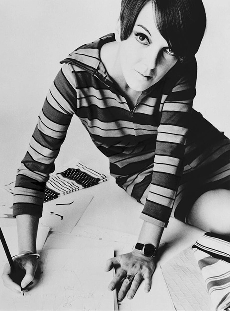Mary Quant sits on the edge of a table sketching designs.
