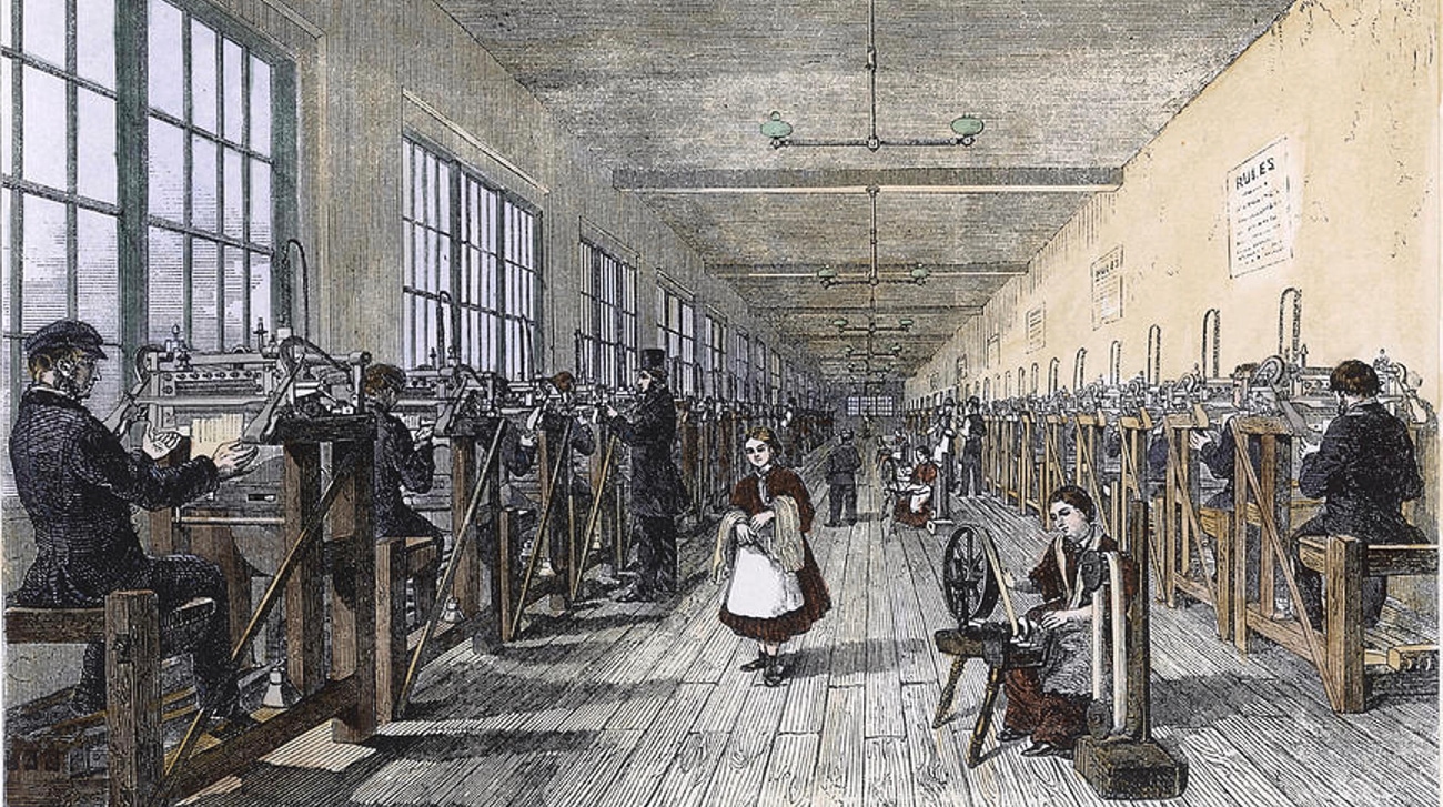 Illustration of a long Victorian stocking factory filled with two rows of men working machines while women spin fibre between them.