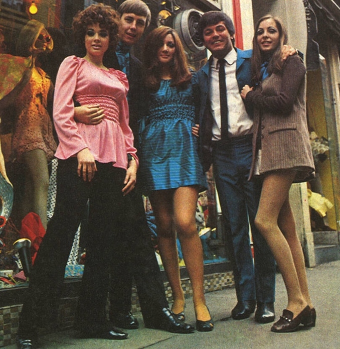 Women wearing mini skirts, silk tops and pants are joined by two men in suits.
