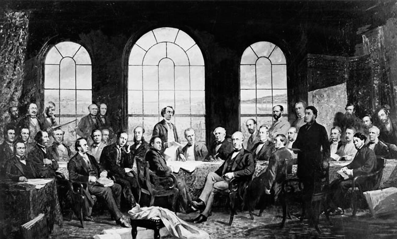 Portrait of the fathers of confederation with John A. McDonald in the centre. The 37 men sit and stand around a large table with three large arched windows behind them. Outside you can see boats on the St. Lawrence River.