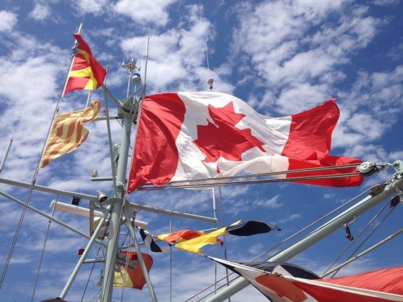 A Canadian flag, raised above a sailboat, waves in the wind.