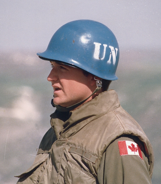 A Canadian peacekeeper wears military fatigues and a blue helmet stenciled with “UN”.
