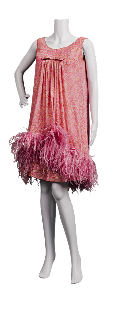 A pink cocktail party dress from the 1960s made of foulard silk shift and chiffon overdress printed with a paisley pattern. It features a loose, A-line cut and short hem over the knee fringed with pink feathers.